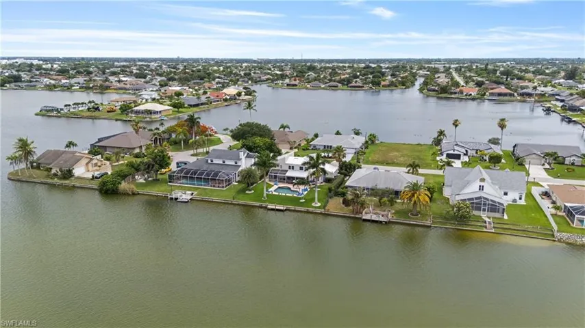 Waterfront property featuring a private dock, screened-in swimming pool, mature palm trees, and a spacious lawn