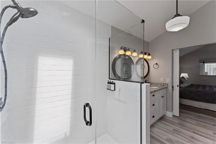 Spacious bathroom featuring a glass-enclosed shower with horizontal white tile, a dark bronze rainfall showerhead, and a vanity with a light-toned countertop, white cabinetry, and circular mirrors