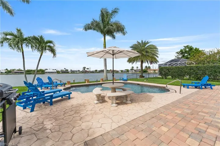 Waterfront backyard with a freeform swimming pool, extensive stamped concrete and paver patio, and mature palm trees