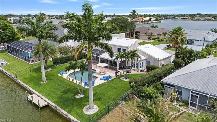 Waterfront property featuring a private boat dock, screened swimming pool, and mature palm trees