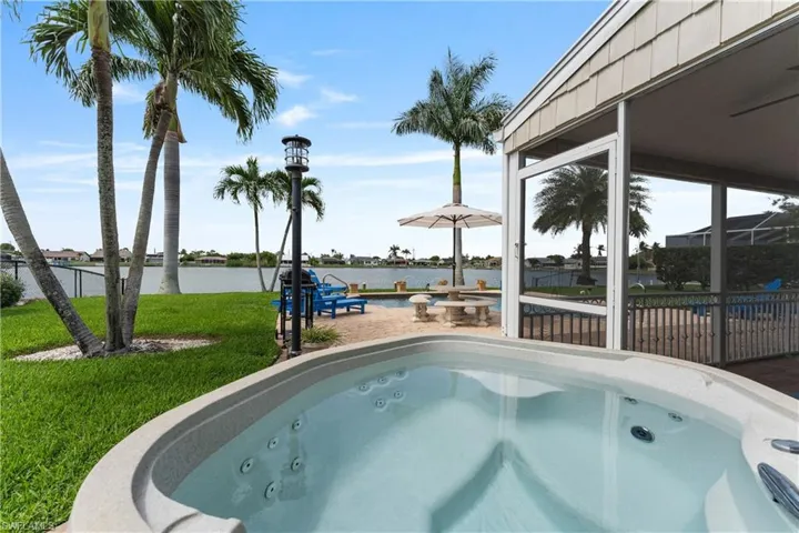 Outdoor hot tub featuring multiple jets, a screened lanai, a paved patio, a manicured lawn, and mature palm trees
