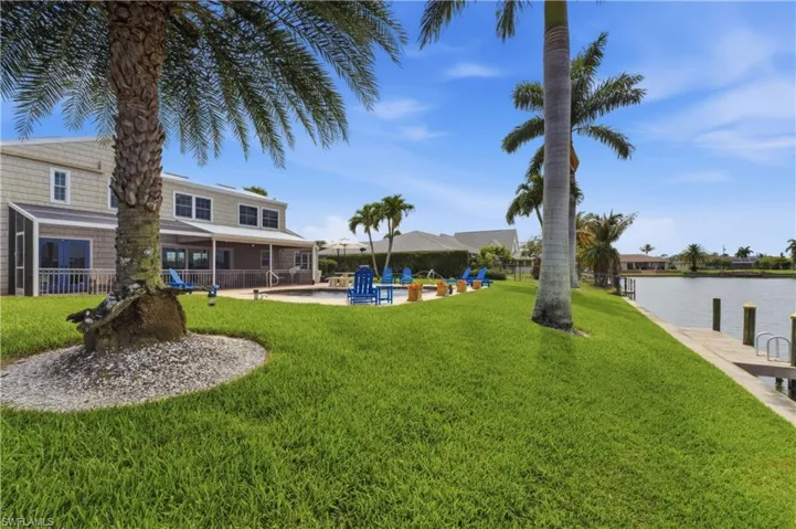 Expansive waterfront property featuring a large green lawn, private boat dock, and mature palm trees