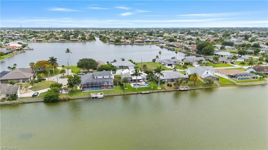 Waterfront property featuring a screened-in pool, private dock, and mature palm trees
