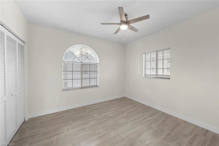 Unfurnished bedroom with a closet, ceiling fan, multiple windows, and wood tiled floors
