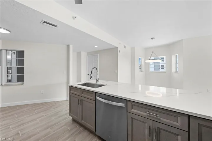 Kitchen with stainless steel dishwasher, pendant lighting, wood tiled floors, light stone countertops, and gray cabinets