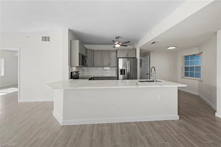 Kitchen with gray cabinets, stainless steel appliances, wood tiled floors, tasteful backsplash, and ceiling fan