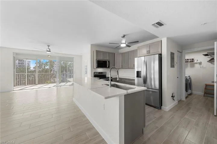 Kitchen with appliances with stainless steel finishes, a ceiling fan, tasteful backsplash, gray cabinets, and light stone countertops