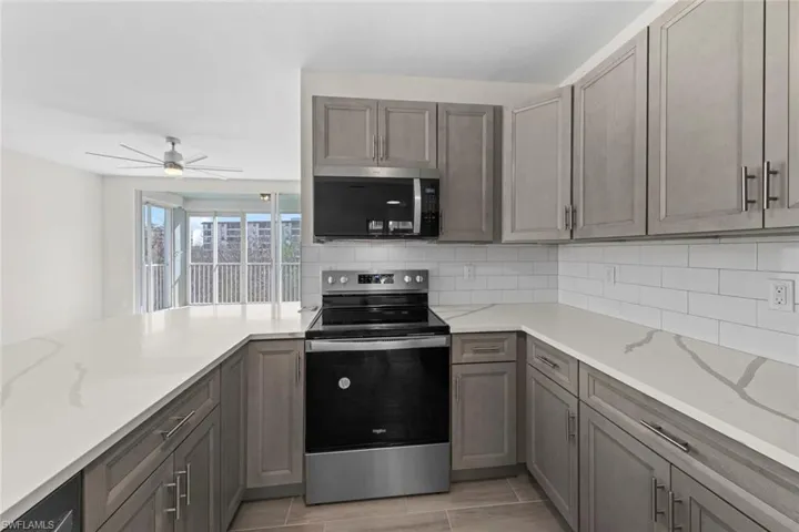 Kitchen featuring appliances with stainless steel finishes, backsplash, light stone counters, ceiling fan, and gray cabinetry