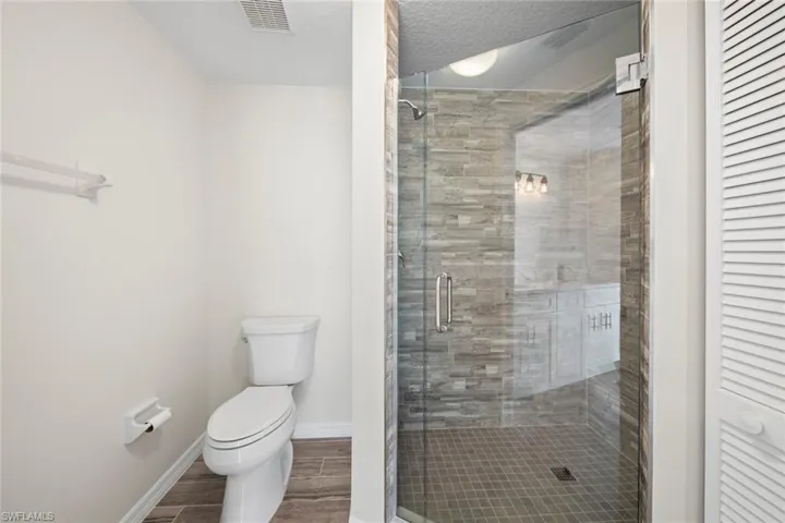 Full bath featuring a shower stall, wood finish floors, a closet, and a textured ceiling