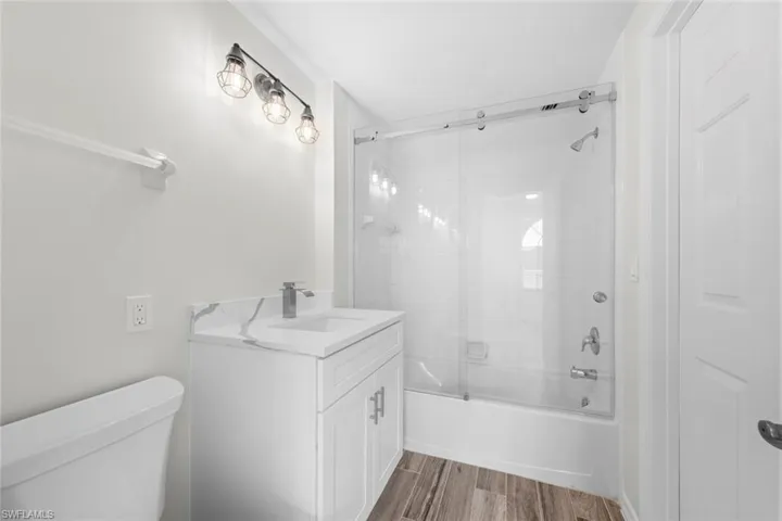 Bathroom featuring enclosed tub / shower combo, light wood-style floors, and vanity