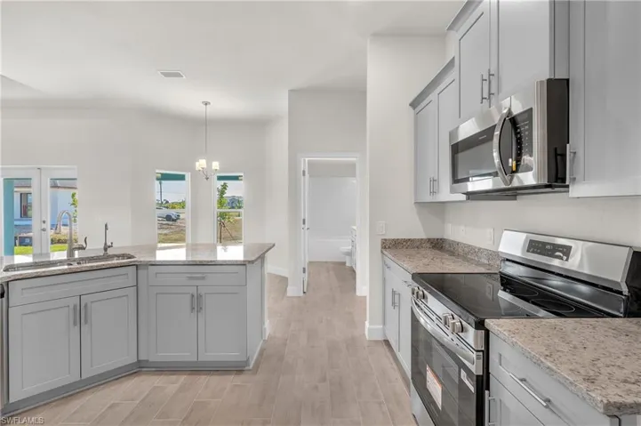 Kitchen featuring stainless steel appliances, a chandelier, gray cabinets, light stone counters, and hanging light fixtures