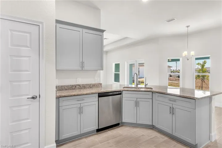 Kitchen with gray cabinetry, a peninsula, light stone countertops, and dishwasher