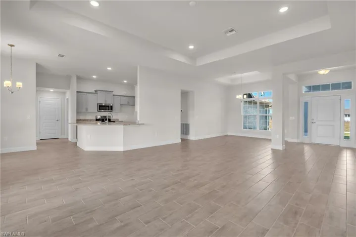 Unfurnished living room with a chandelier, a tray ceiling, recessed lighting, and wood tiled floors