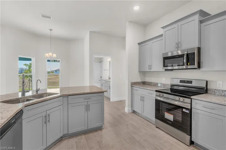 Kitchen with appliances with stainless steel finishes, gray cabinets, light stone countertops, hanging light fixtures, and a chandelier