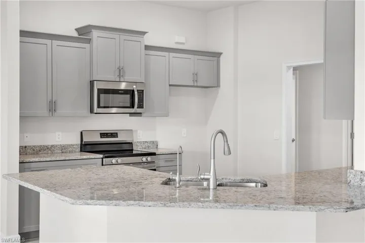 Kitchen featuring appliances with stainless steel finishes, gray cabinetry, light stone counters, and a peninsula