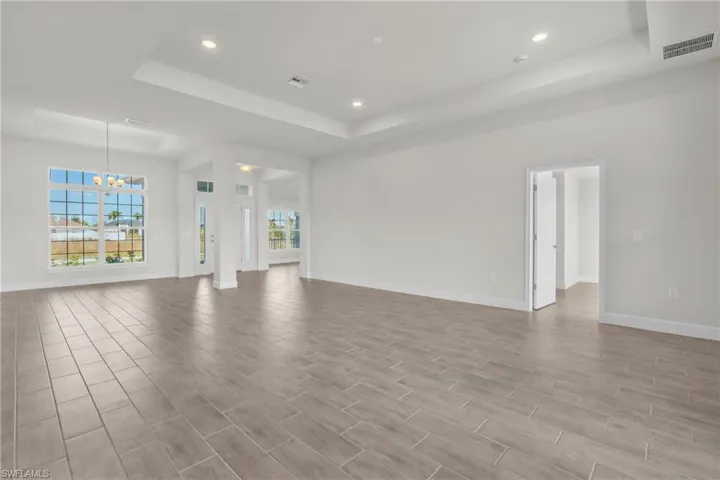 Unfurnished living room featuring a chandelier, a raised ceiling, wood finish floors, and recessed lighting