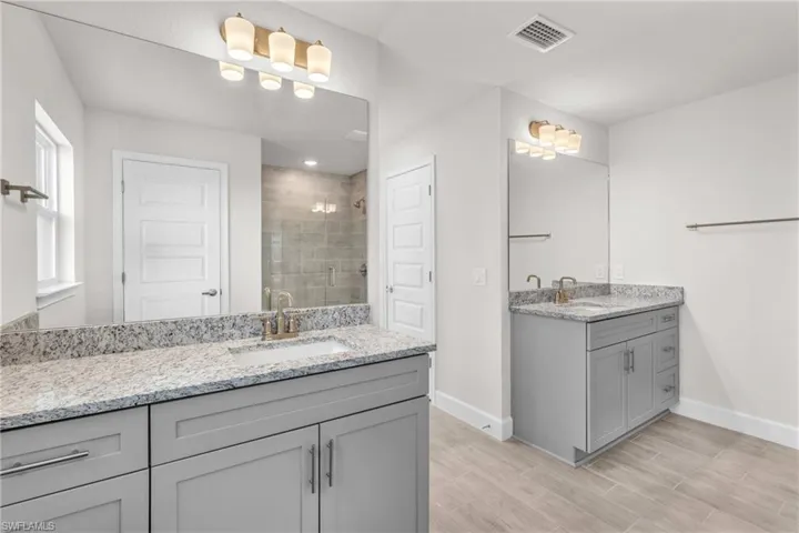 Bathroom with two vanities, a stall shower, and wood finish floors