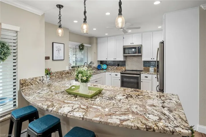 Kitchen with appliances with stainless steel finishes, white cabinets, kitchen peninsula, ceiling fan, and ornamental molding