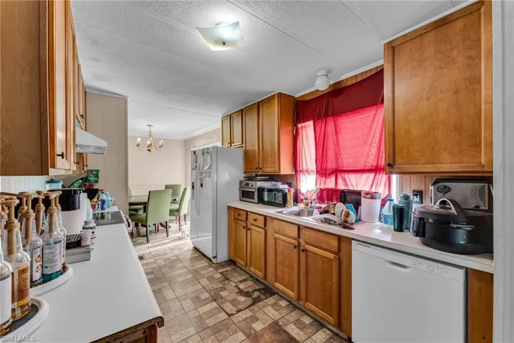 Kitchen with sink, white appliances, hanging light fixtures, a notable chandelier, and a textured ceiling