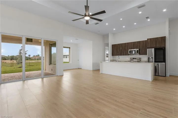 Kitchen with appliances with stainless steel finishes, light hardwood / wood-style flooring, dark brown cabinetry, an island with sink, and ceiling fan