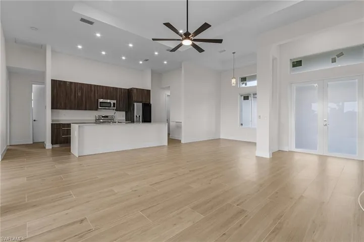 Unfurnished living room with light hardwood / wood-style flooring, french doors, a towering ceiling, and ceiling fan