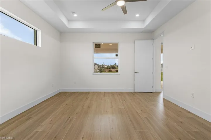 Spare room with light wood-type flooring, ceiling fan, and a raised ceiling