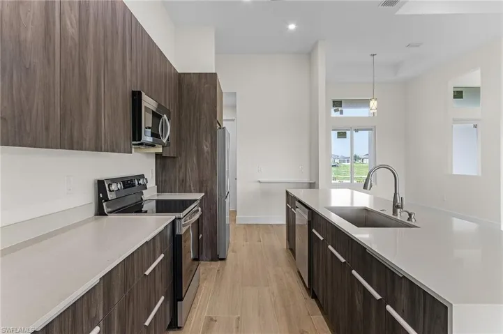 Kitchen with light hardwood / wood-style flooring, dark brown cabinets, stainless steel appliances, decorative light fixtures, and sink