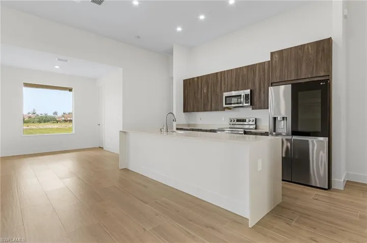 Kitchen with stainless steel appliances, sink, dark brown cabinets, a kitchen island with sink, and light wood-type flooring