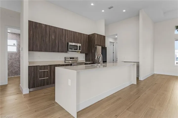 Kitchen with appliances with stainless steel finishes, light hardwood / wood-style flooring, and a kitchen island with sink