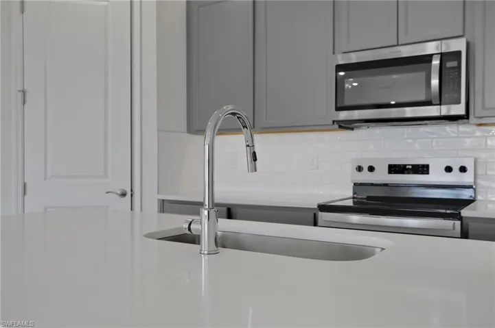 Kitchen featuring gray cabinetry, stainless steel appliances, light stone countertops, and tasteful backsplash