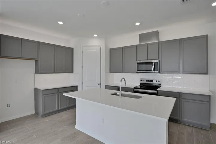 Kitchen featuring stainless steel appliances, wood tiled floors, a center island with sink, gray cabinets, and recessed lighting