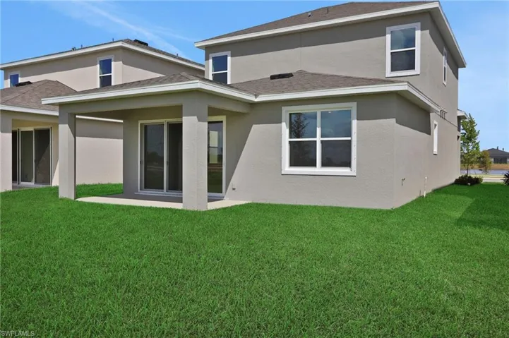 Back of house with a lawn, a patio, stucco siding, and roof with shingles
