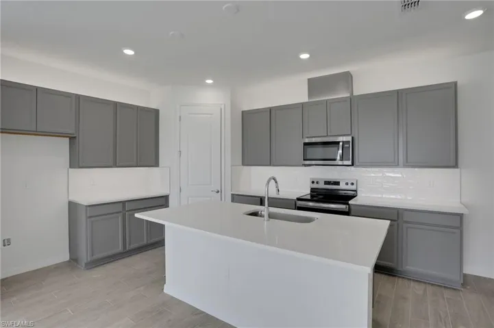 Kitchen featuring gray cabinets, stainless steel appliances, a center island with sink, wood tiled floors, and recessed lighting