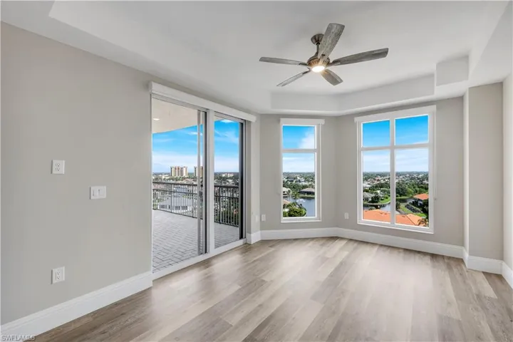 Bedroom #3 featuring wood-finish flooring, a tray ceiling with a ceiling fan, and large windows
