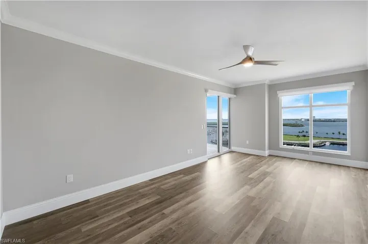 Spacious primary suite with waterfront views featuring wood-finish flooring, a contemporary ceiling fan, and crown molding