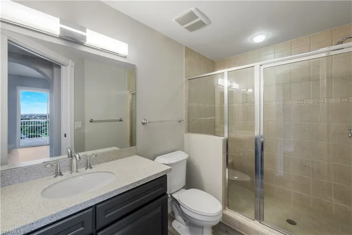En suite bathroom for bedroom #2 featuring a single vanity with dark cabinetry, a light speckled countertop, and an oval undermount sink