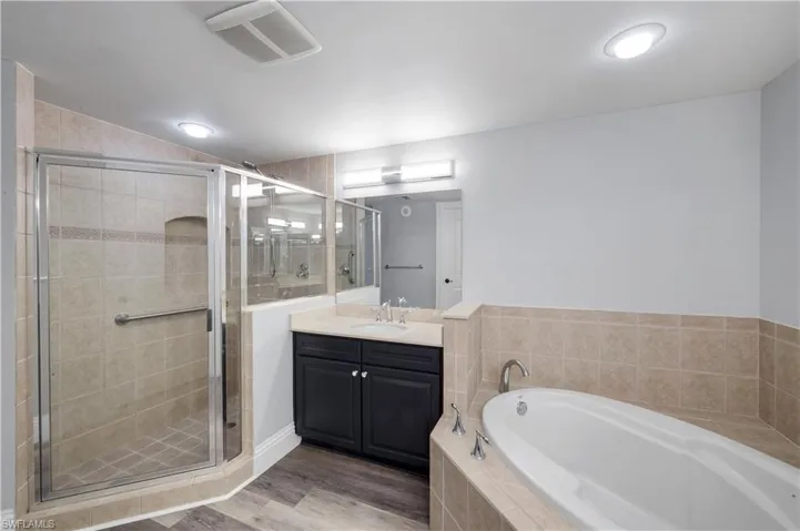 Primary bathroom featuring a glass-enclosed shower, a built-in soaking tub, a dark wood-finish vanity with a light-toned countertop, and wood-finish plank flooring