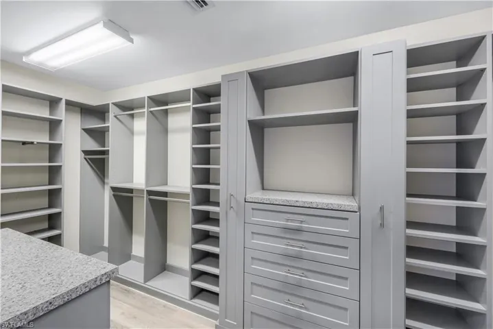 Custom-built primary suite walk-in closet #1 featuring extensive built-in shelving, multiple hanging rods, closed cabinetry, a central island, and drawer storage