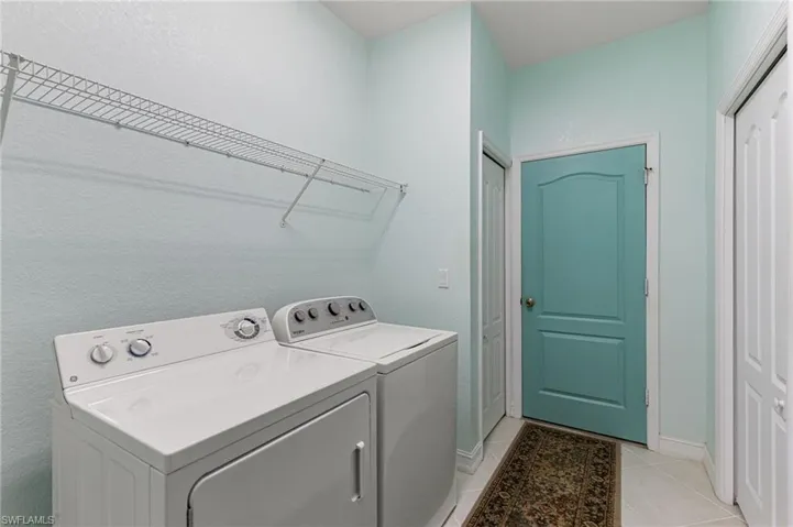 Laundry area featuring washing machine and clothes dryer, a textured wall, and light tile patterned floors
