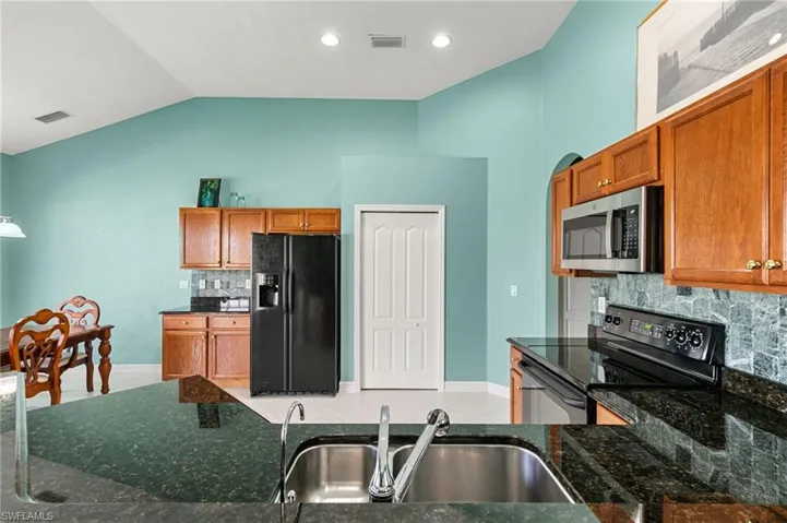 Kitchen with black appliances, decorative backsplash, light tile patterned flooring, dark stone countertops, and wood finish cabinetry