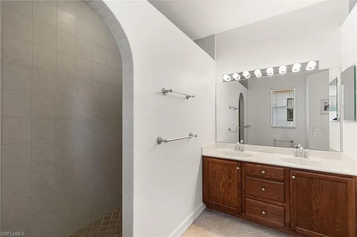 Full bath featuring double vanity, light tile patterned floors, and a walk in shower