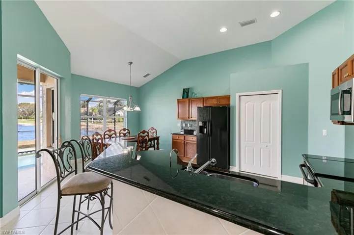 Kitchen with black appliances, wood finish cabinets, vaulted ceiling, dark stone counters, and light tile patterned flooring