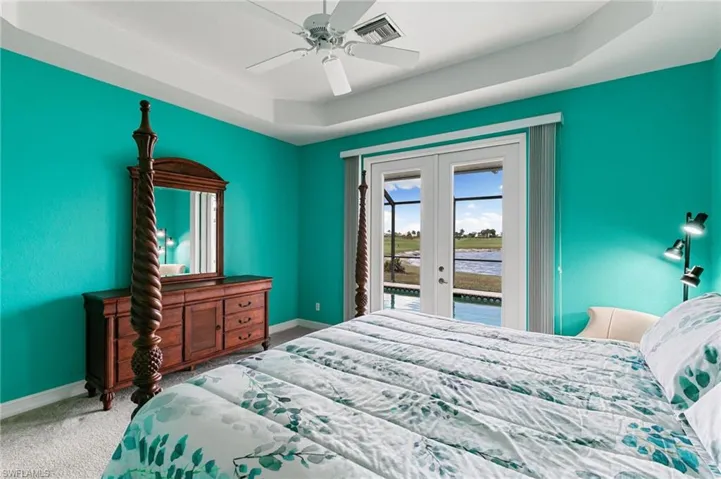 Carpeted bedroom featuring french doors, a tray ceiling, access to outside, a water view, and a ceiling fan