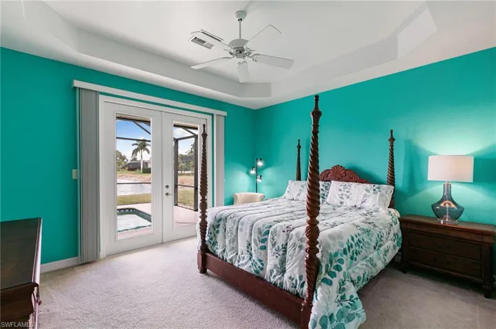 Carpeted bedroom featuring french doors, a tray ceiling, access to exterior, and ceiling fan