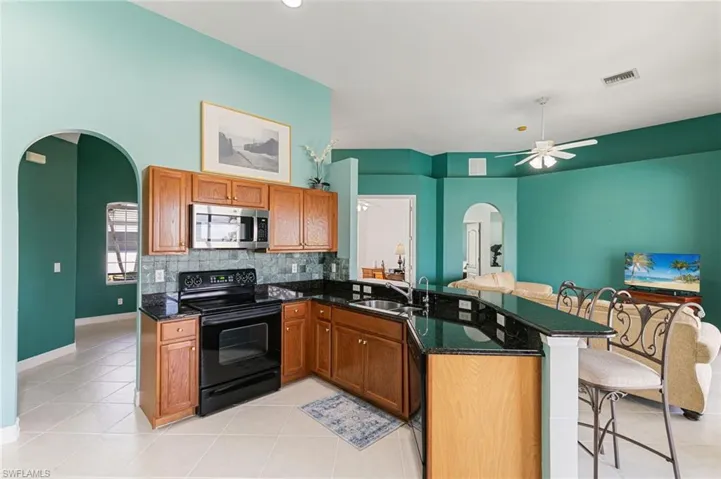 Kitchen with arched walkways, a kitchen bar, a peninsula, black appliances, and wood finish cabinetry