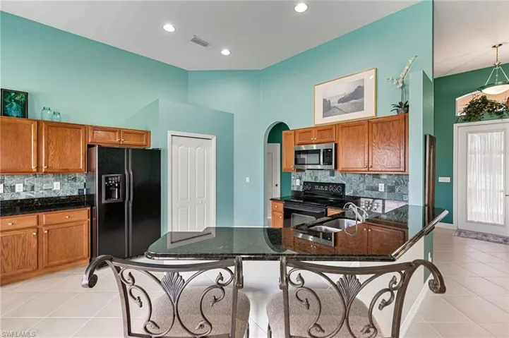 Kitchen with light tile patterned flooring, decorative backsplash, arched walkways, and dark stone countertops
