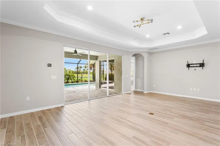 Unfurnished room with a raised ceiling, arched walkways, light wood finished floors, ornamental molding, and ceiling fan