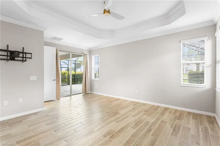 Empty room with a raised ceiling, ceiling fan, light wood-style flooring, and crown molding