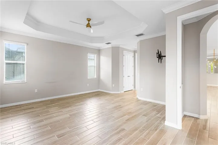 Unfurnished room with a raised ceiling, arched walkways, ceiling fan, light wood finished floors, and plenty of natural light