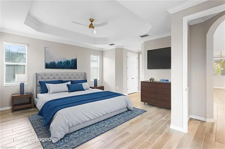 Bedroom with arched walkways, a raised ceiling, light wood-type flooring, multiple windows, and ornamental molding